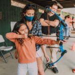 Woman in Orange Shirt Holding Bow and Arrow